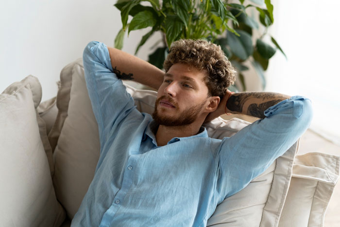 A relaxed jobless bf lounging on a sofa with hands behind his head.