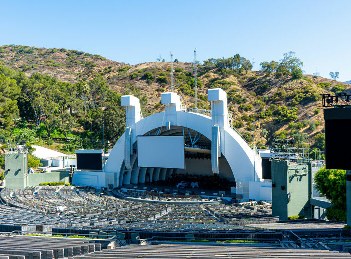An empty outdoor amphitheater, the Hollywood Bowl, surrounded by green hills, awaits a Miley Cyrus performance.