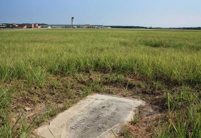 Gravestone in tall grass with an airport in the background, telling the story of the buried couple Gravestone in tall grass with an airport in the background, telling the story of the buried couple
