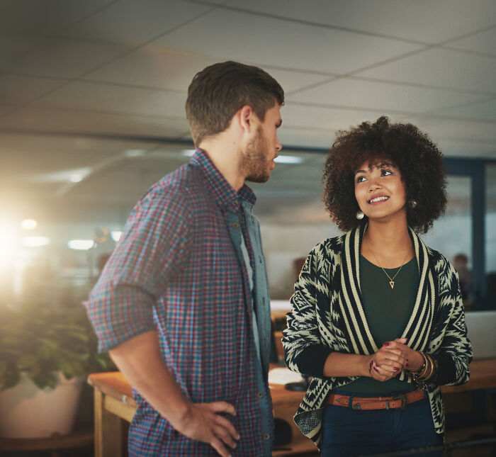 Two colleagues in an office talking, with the woman smiling, symbolizing people who overheard conversations.