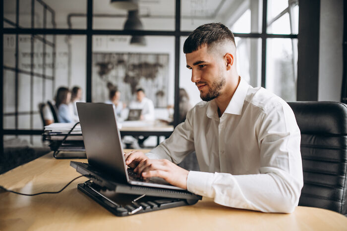 A male colleague typing on his laptop in a modern office setup.