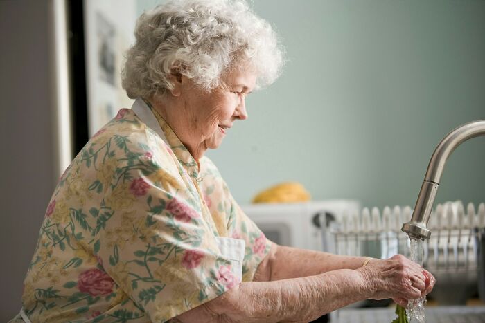 Elderly woman washes hands, a scene showing how strange patients might struggle with basic hygiene.