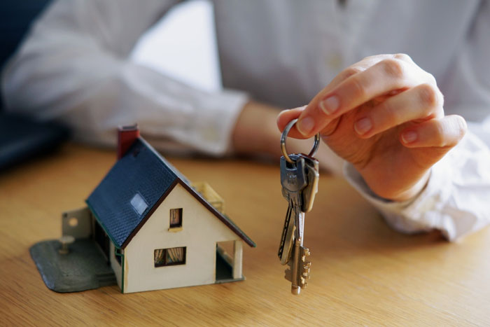 Parents give son free housing; a hand holds keys next to a small house model, symbolizing a future home.
