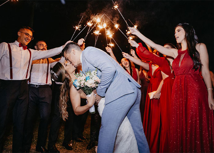 A newlywed couple shares a kiss, surrounded by friends and family holding sparklers at a child-free celebration.