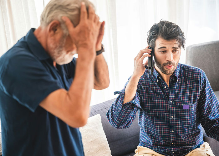 A man on the phone with a distressed older man in the background, showing tension over special exceptions.