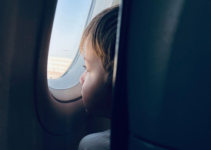 A young child looking out of an airplane window seat, highlighting the struggle over airplane window seats for kids. A young child looking out of an airplane window seat, highlighting the struggle over airplane window seats for kids.