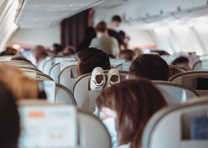 An airplane interior shows rows of seats, with a pair of baby shoes visible on the seatback in front. An airplane interior shows rows of seats, with a pair of baby shoes visible on the seatback in front.