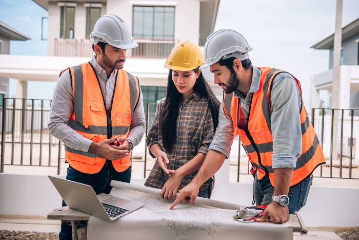 Three engineers discussing a blueprint, depicting satisfying stories of teamwork and construction.