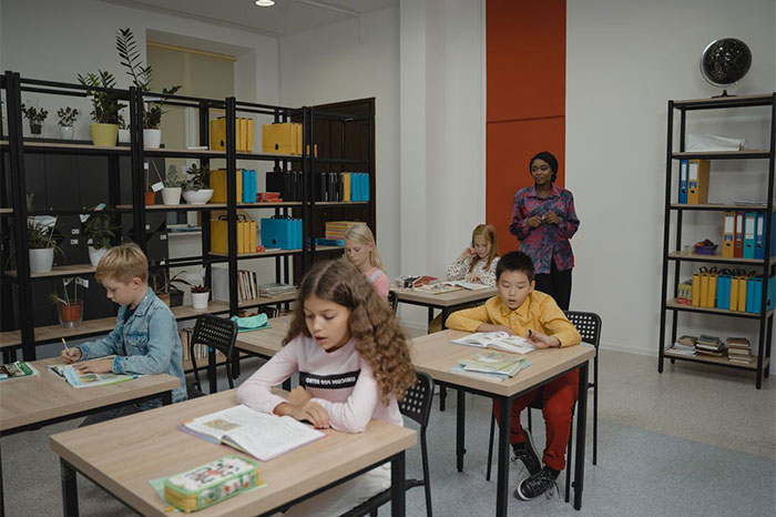 A diverse group of students in a classroom with a teacher, all focused on their desks. A diverse group of students in a classroom with a teacher, all focused on their desks.