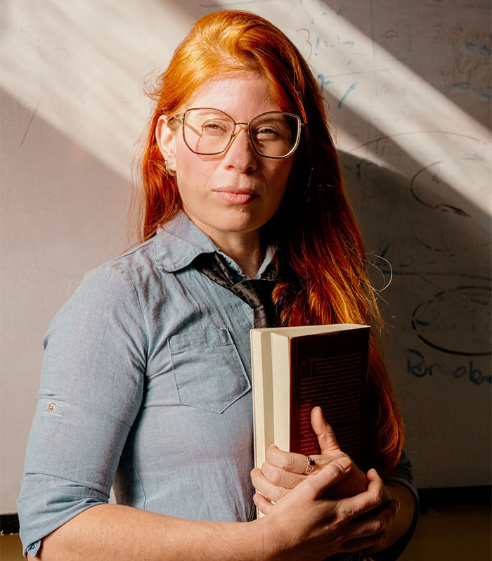 A teacher with long red hair and glasses holding two books, looking directly at the camera. This teacher is driven crazy by a student. The student finds a perfect way to drive her teacher crazy. A teacher with long red hair and glasses holding two books, looking directly at the camera. This teacher is driven crazy by a student. The student finds a perfect way to drive her teacher crazy.