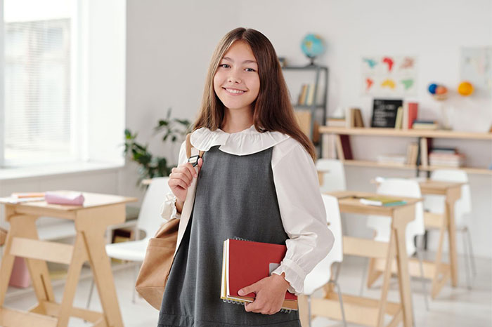 A smiling student holding books in a classroom, looking at the camera, a student finding a perfect way to drive her teacher crazy. A smiling student holding books in a classroom, looking at the camera, a student finding a perfect way to drive her teacher crazy.
