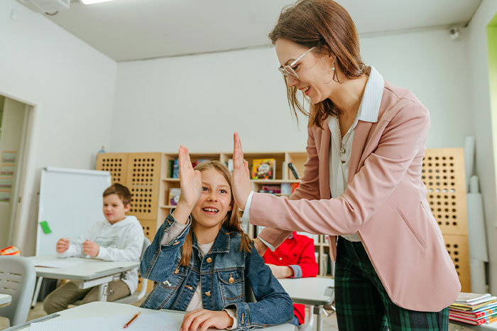 A teacher giving a high-five to a smiling student in a classroom, showing a student's perfect way to drive her teacher crazy. A teacher giving a high-five to a smiling student in a classroom, showing a student's perfect way to drive her teacher crazy.
