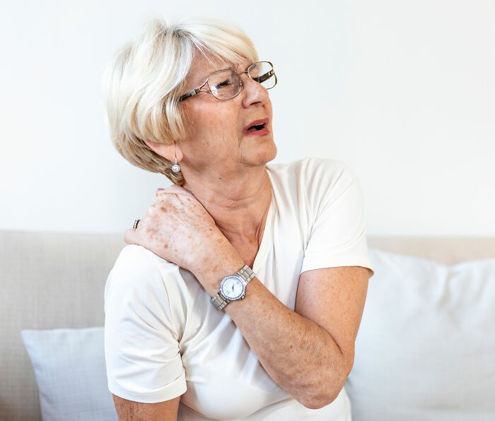 An older woman rubbing her shoulder due to pain, a common health symptom among seniors.