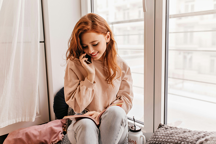 A smiling young woman on her cell phone, unaware of a fake friend taking advantage of her.