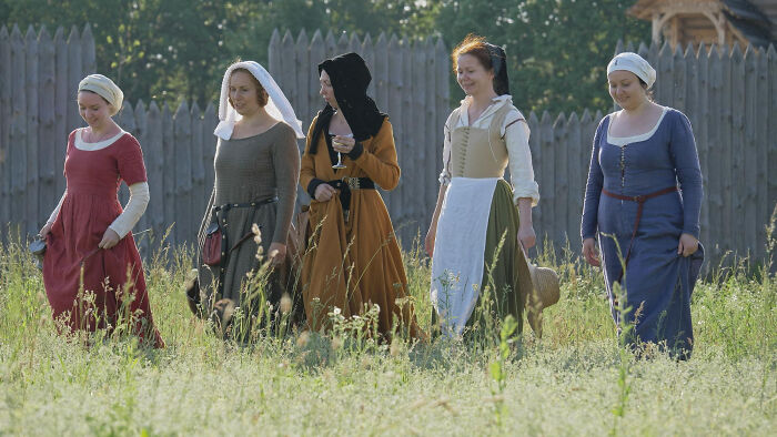 Five women in historical clothing walking through a grassy field, representing historical facts.