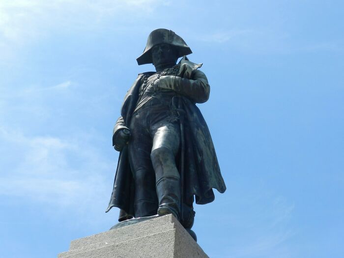 Historical facts: A bronze statue of Napoleon Bonaparte against a clear blue sky, a figure surrounded by beliefs.