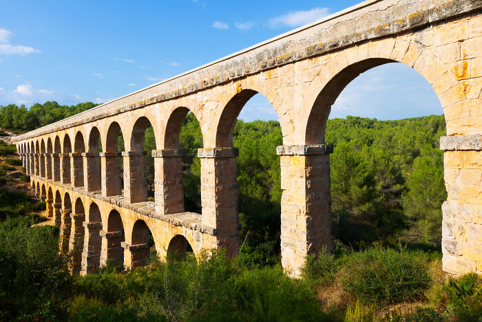 A historical facts aqueduct with many arches spanning a green forest, illustrating historical facts.