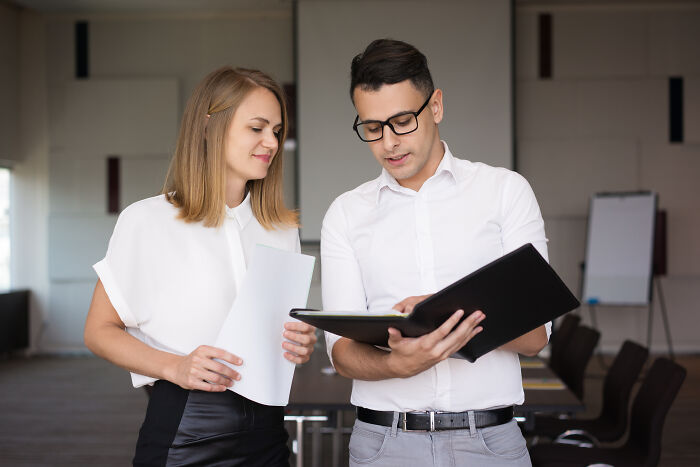 A female office worker holds documents while a male colleague looks on, representing subtle sexism.