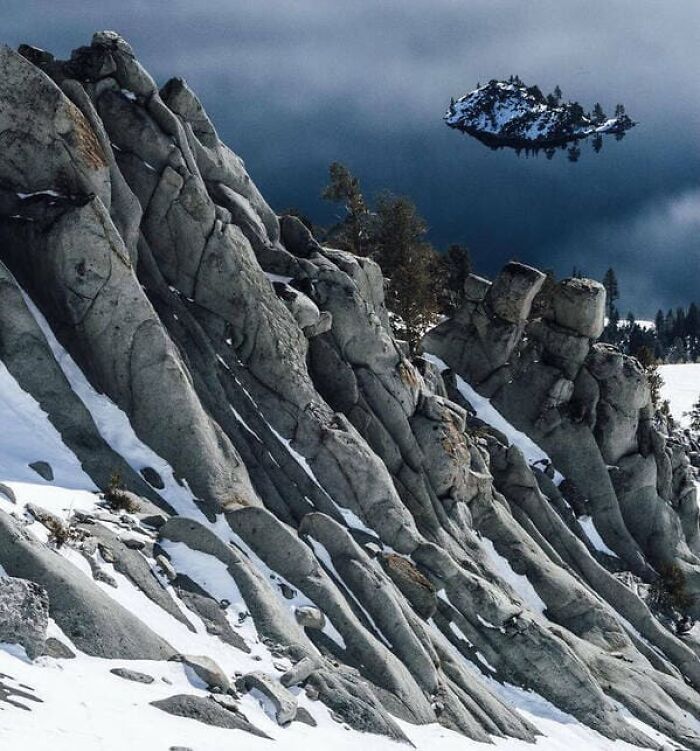 Rocky, snowy cliffs look down on a dark lake where an island appears to float in the sky.
