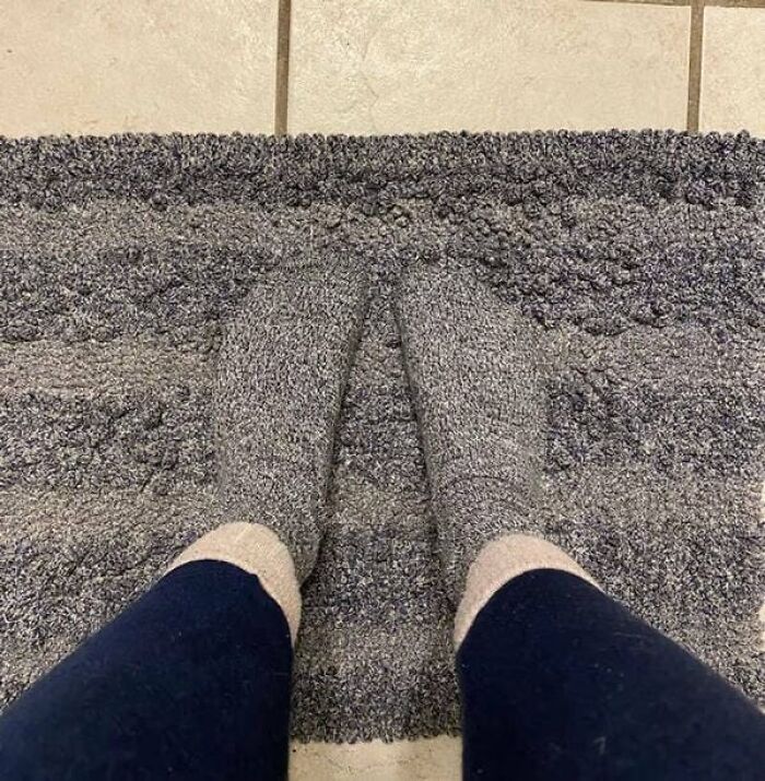 A person wears grey textured socks that perfectly match the pattern of a grey woven rug.