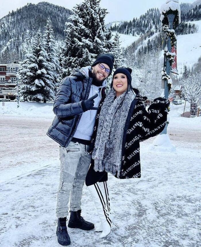 A couple posing in a snowy landscape with a confusing perspective of the woman standing on one leg