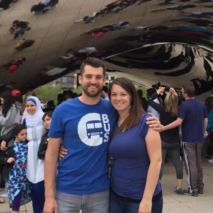 A smiling couple posing in front of the Cloud Gate sculpture, with people reflected above them.