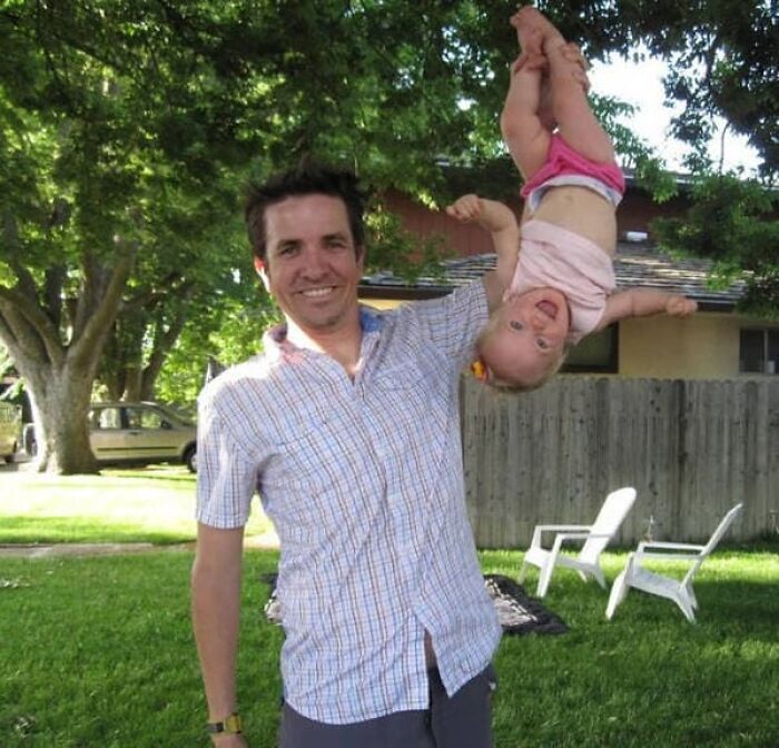 A happy father holding his baby upside down in the backyard, creating a fun family perspective.