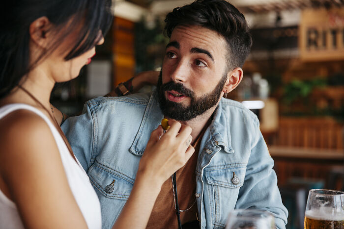 A man with a beard talking to a woman, discussing dating red flags in a casual setting.