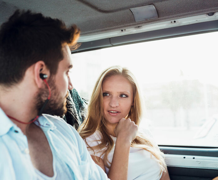 A woman looks cautiously at a man in a car, displaying potential dating red flags.