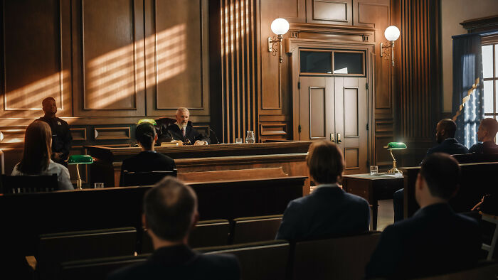 A view from behind of people in a courtroom listening to a judge during a trial