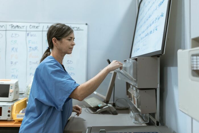 A female nurse in blue scrubs organizing medical files at her workspace station