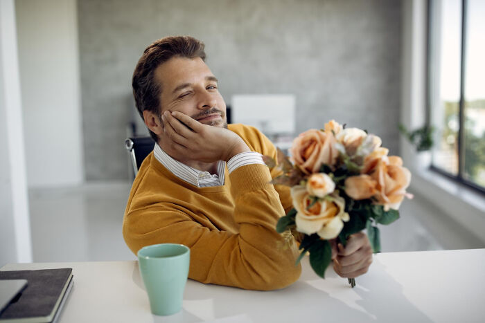 A male coworker holding flowers and winking, hinting at unprofessional workplace comments.