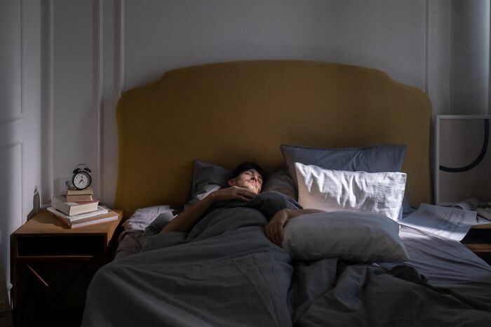 A tired male coworker sleeping deeply in a bed, illustrating exhaustion after a long day at work
