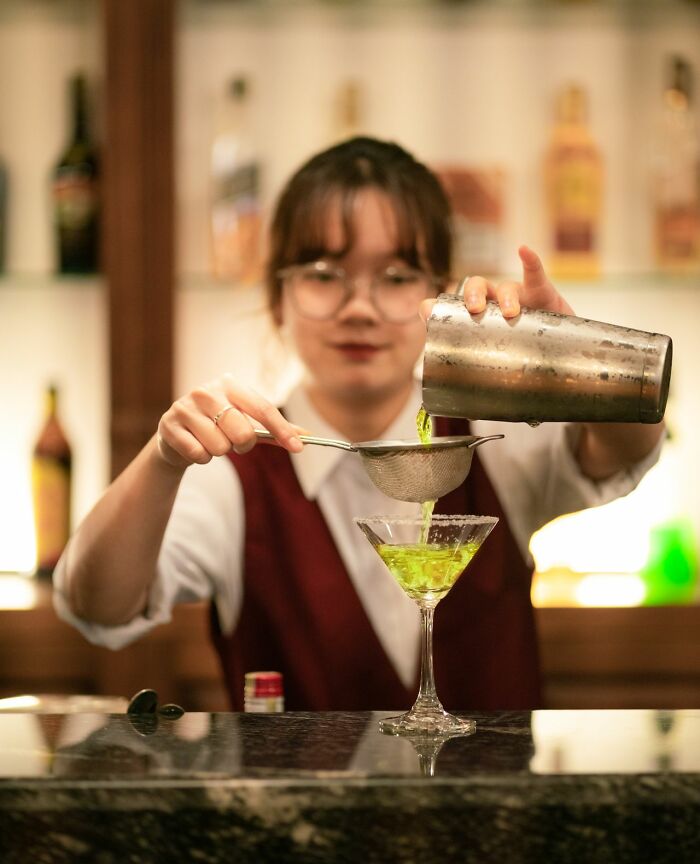 A bartender pouring a green drink through a strainer in a bar