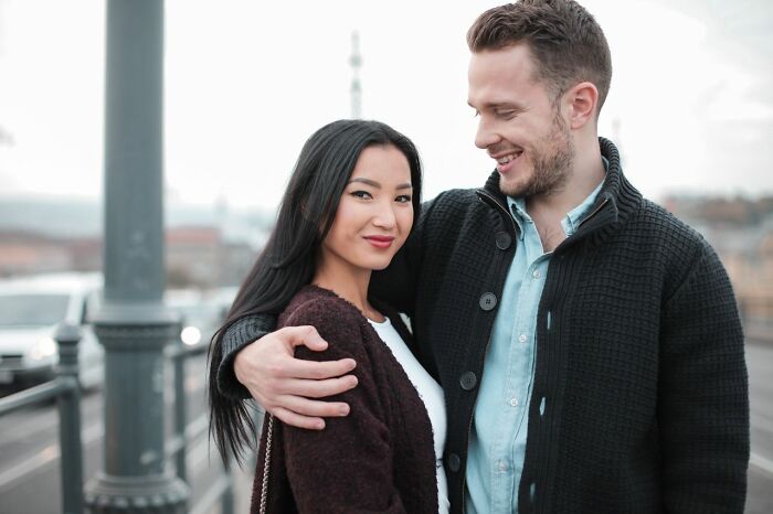 A male coworker smiling as he puts his arm around a female colleague on a city street