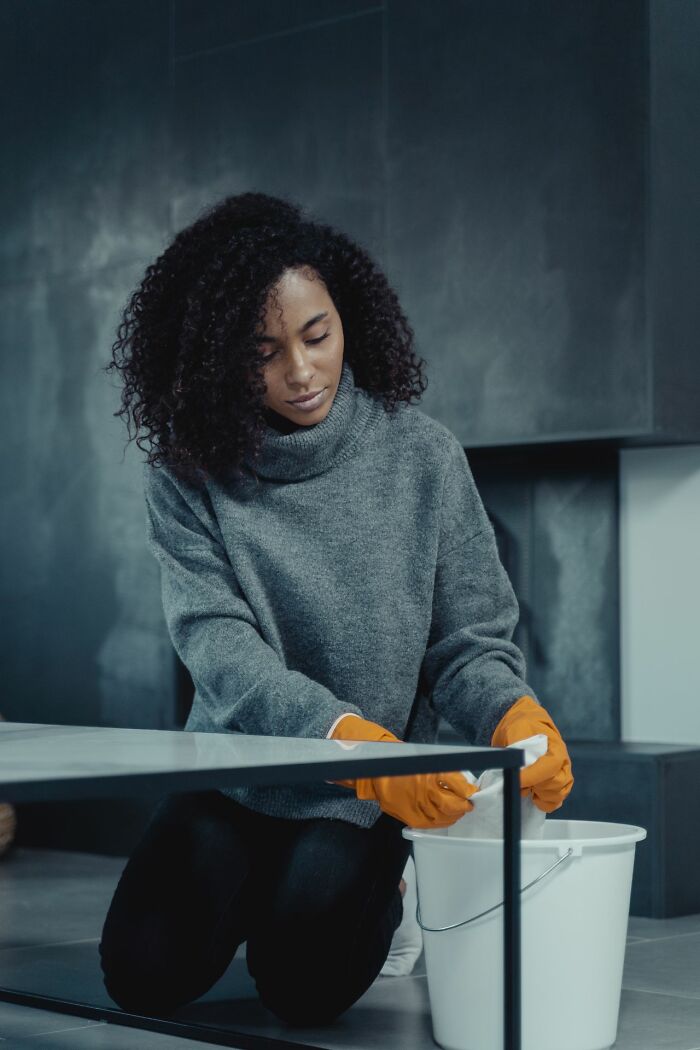 A female worker with curly hair wearing orange gloves while cleaning a table at the office
