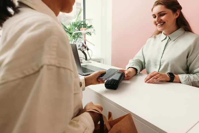 A female cashier smiling while a customer pays using a smartphone, showing daily female coworker interactions