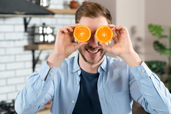 A man playfully holding orange slices over his eyes, relating to stories shared by women.
