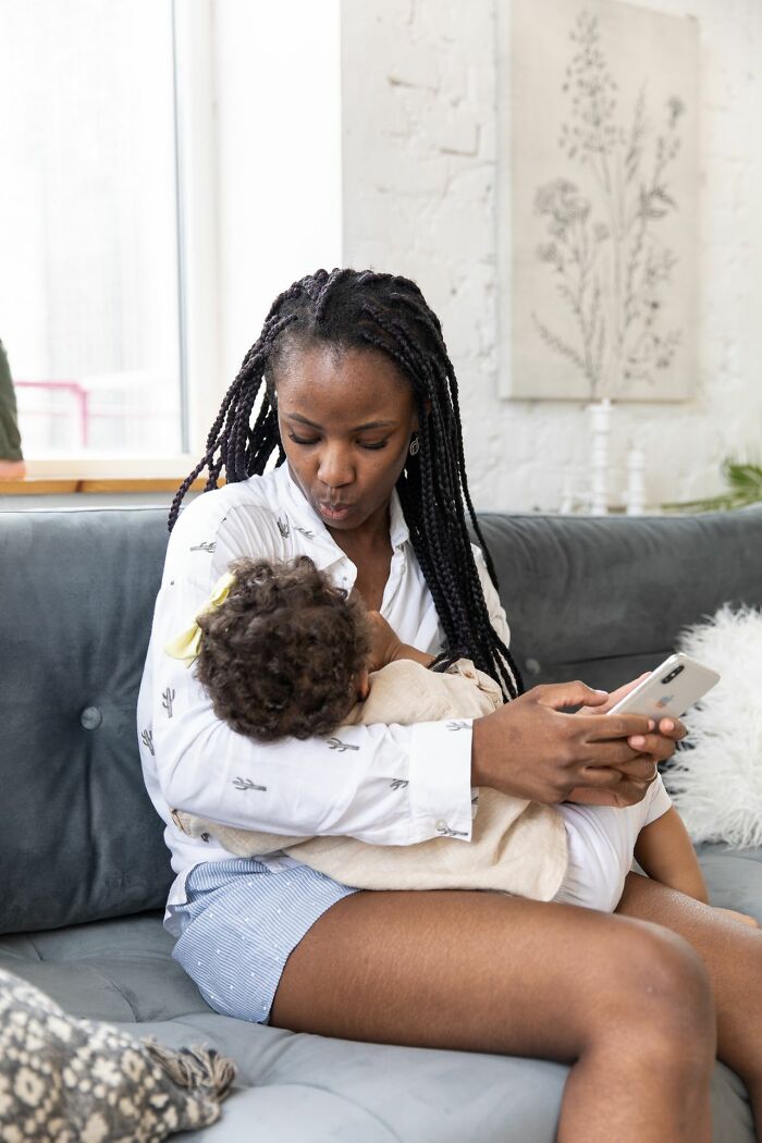 A mother holding her baby on a couch, showing the experiences of women and male coworkers.