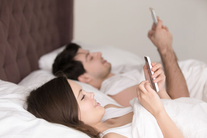 A couple lying in bed, secretly looking at their phones, hiding creepy things they did to a partner