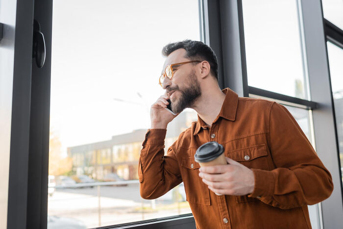 A smiling man on a phone call near a window, talking about a partner.