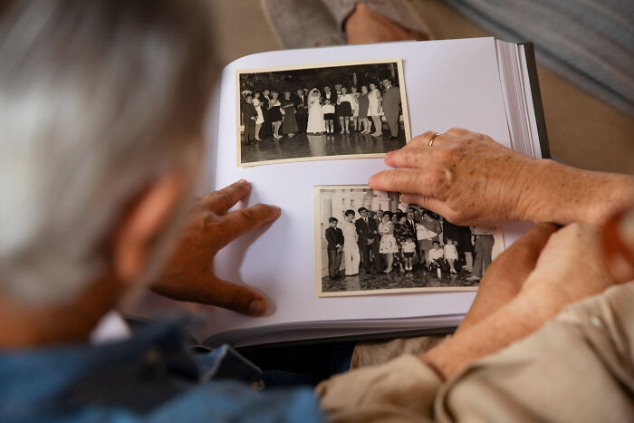 Hands of an elderly couple viewing old black and white photographs, symbolizing memories they never plan to confess.