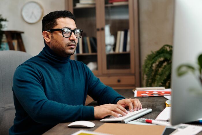 A focused man in a blue turtleneck working on his computer, hiding secrets he did to a partner