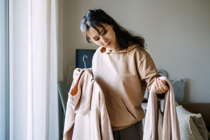 A woman holding up similar-looking hoodies, symbolizing creepy habits with a partner.