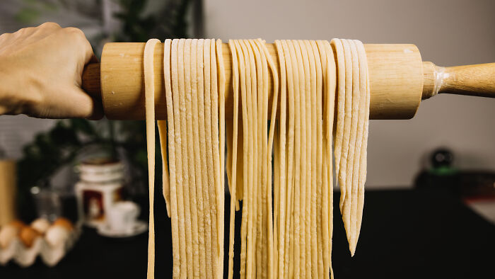 Freshly made pasta noodles draped over a rolling pin, a surprising thing wealthy people buy.