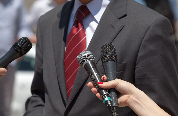 A professional in a suit and tie being interviewed by reporters, discussing industry secrets widely known among professionals.