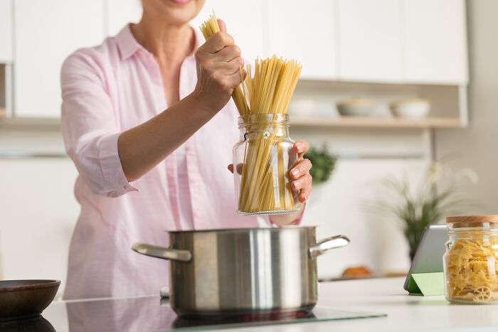 Person cooking pasta adding spaghetti to pot in kitchen