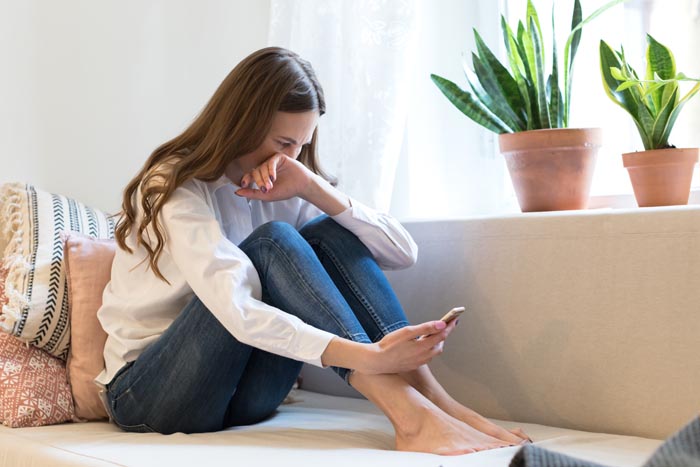 A crying woman sits on a couch, looking at her phone, experiencing a relationship nightmare. A crying woman sits on a couch, looking at her phone, experiencing a relationship nightmare.