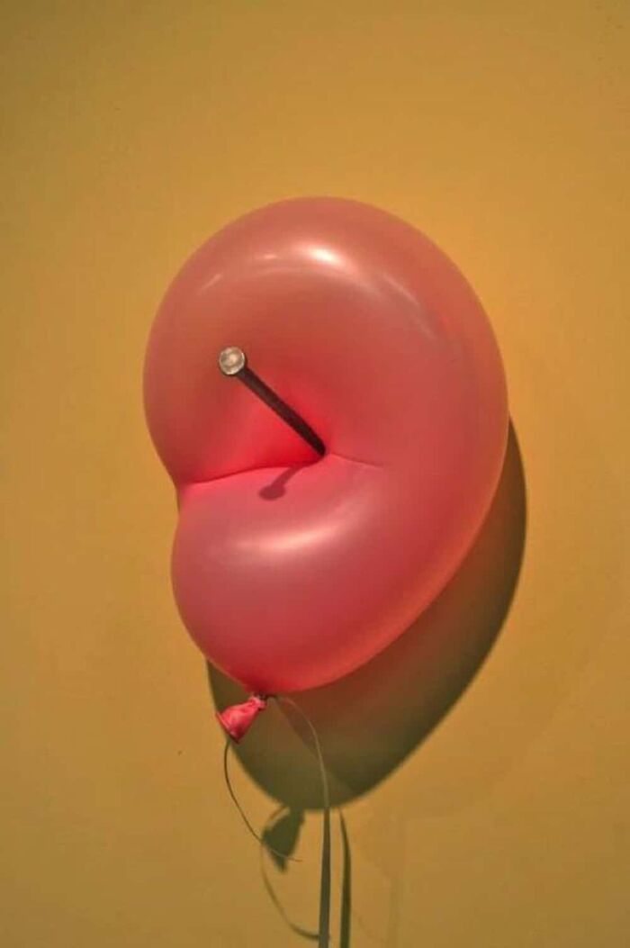 A pink balloon with a nail seemingly piercing it without popping, creating a baffling image that defies physical sense.