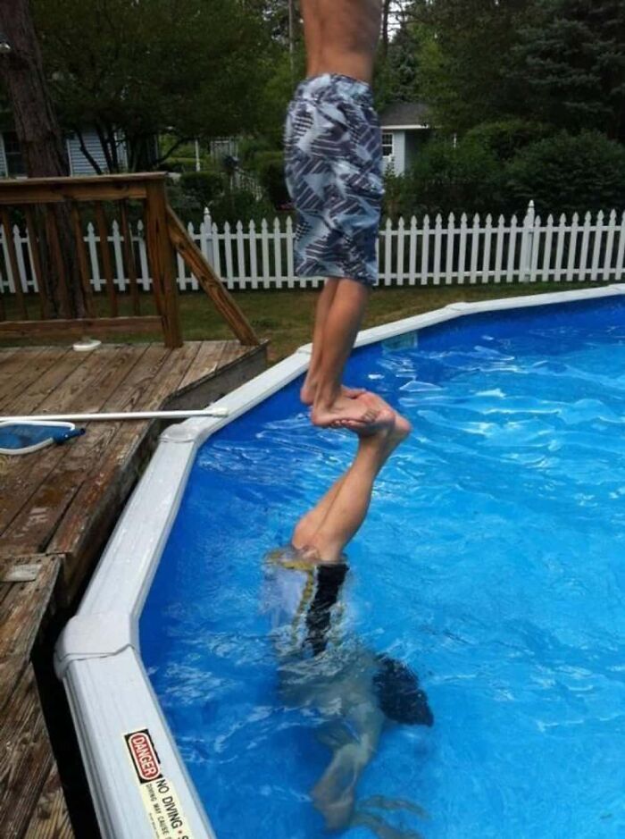 A baffling image of a person seemingly standing on top of another persons head underwater in a swimming pool.